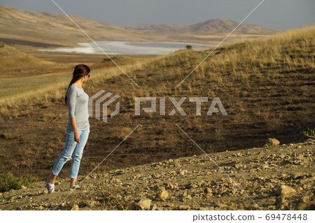 Young woman with long hair standing elegant in the middle of desert field on background of mountains, view from side Young woman with long hair standing elegant in the middle of desert field on background of mountains, view from side 69478448