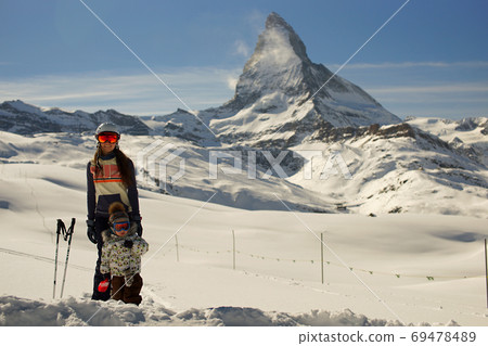 Young smiling woman and little child standing in deep snow on backgroung of Matterhorn Switzerland. Happy family 69478489