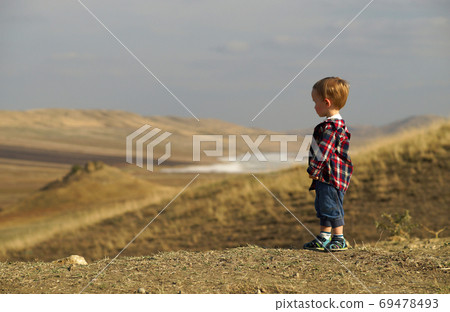 Side portrait of little boy standing lonely and looking into the distance in yellow desert field Side portrait of little boy standing lonely and looking into the distance in yellow desert field 69478493