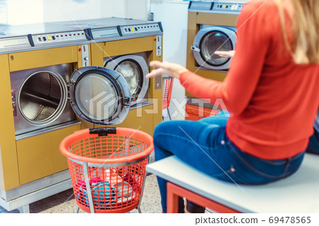 Woman sits astonished in front of washing machine in laundromat Woman sits astonished in front of washing machine in laundromat 69478565