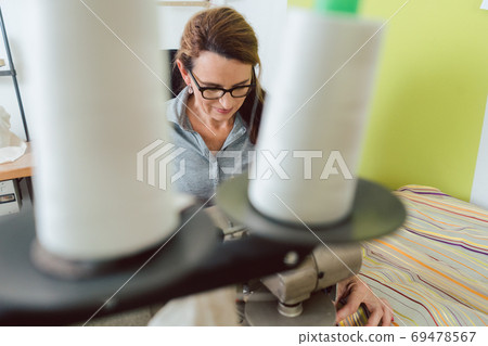 Seamstress sews deco fabric on sewing machine in tailoring Seamstress sews deco fabric on sewing machine in tailoring 69478567