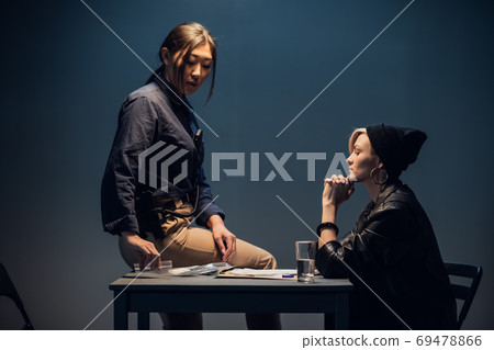 A young investigator an asian woman sits on a table during the interrogation of a pretty criminal A young investigator an asian woman sits on a table during the interrogation of a pretty criminal 69478866