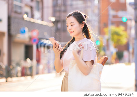 A young woman on the way home from shopping with a smartphone in the city A young woman on the way home from shopping with a smartphone in the city 69479184