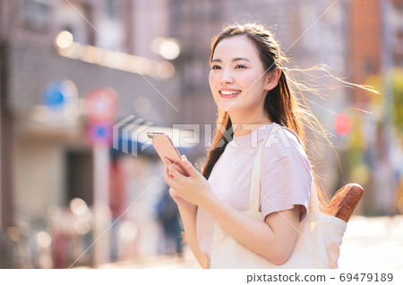 A young woman on the way home from shopping with a smartphone in the city A young woman on the way home from shopping with a smartphone in the city 69479189