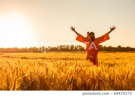 African woman in traditional clothes standing arms raised in field sunset or sunrise African woman in traditional clothes standing arms raised in field sunset or sunrise 69479373