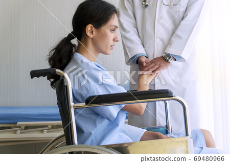 Patient young woman unwell sitting on wheelchair while doctor ma 69480966