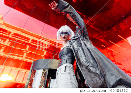 Stylish futuristic blonde in cyberpunk style on a red mirror background. 69481212