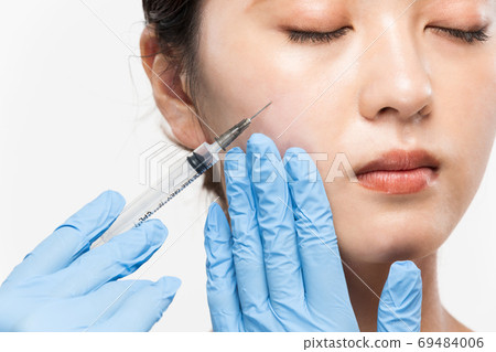 A syringe is placed on a woman's cheek A syringe is placed on a woman's cheek 69484006