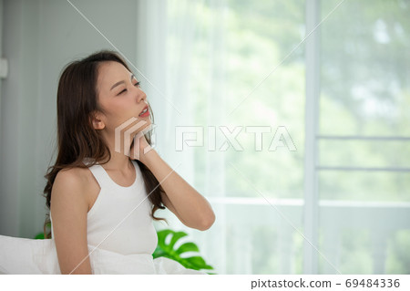 young Asian woman sitting on bed has neck pain after wake up in the morning,Healthcare Concept 69484336