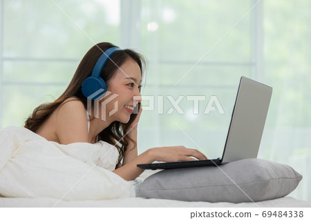 Beautiful Attractive Asian young woman listen music and lying on bed looking on computer laptop in bedroom feeling so relax and comfortable at home,lifestyle in bedroom Concept,Selective Focus Beautiful Attractive Asian young woman listen music and lying on bed looking on computer laptop in bedroom feeling so relax and comfortable at home,lifestyle in bedroom Concept,Selective Focus 69484338