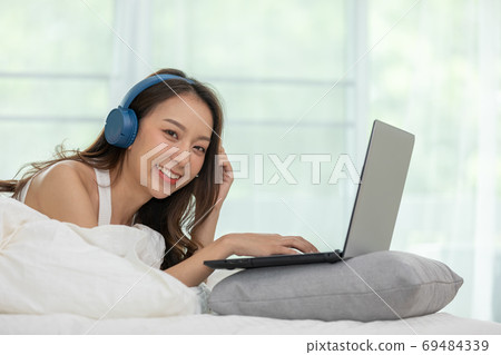 Beautiful Attractive Asian young woman listen music and lying on bed looking on computer laptop in bedroom feeling so relax and comfortable at home,lifestyle in bedroom Concept,Selective Focus Beautiful Attractive Asian young woman listen music and lying on bed looking on computer laptop in bedroom feeling so relax and comfortable at home,lifestyle in bedroom Concept,Selective Focus 69484339