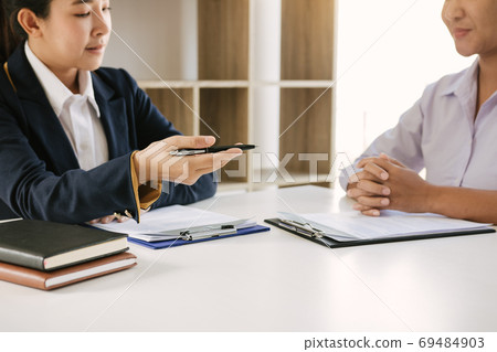 Asian young adult sitting at desk across from manager being inte Asian young adult sitting at desk across from manager being inte 69484903