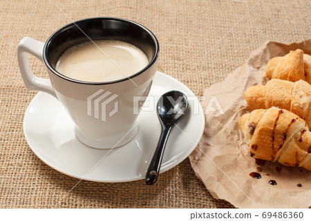 Cup of black coffee with fresh croissants on wrapping paper Cup of black coffee with fresh croissants on wrapping paper 69486360