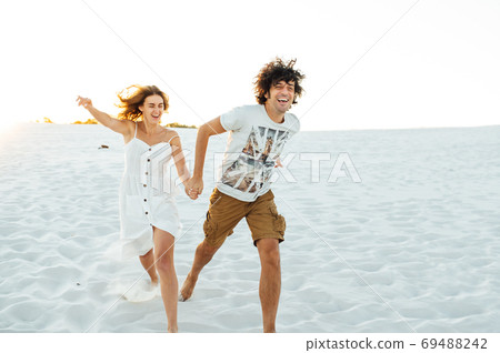 Cheerful couple in love running on the beach and enjoying their vacation Cheerful couple in love running on the beach and enjoying their vacation 69488242