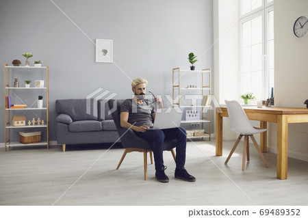 Smiling man sitting on chair with laptop and working online at home 69489352