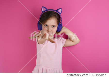 Beautiful little girl listening to music on color background. Pink clothes and a purple gadget. The 69495044