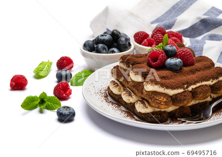 portion of Classic tiramisu dessert with raspberries and blueberries on ceramic plate isolated on white 69495716