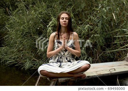 Beautiful young woman in dress meditating on the nature 69498000