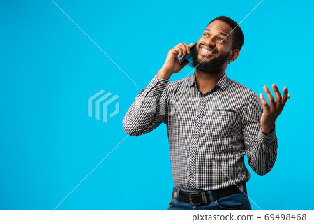 Smiling black guy talking on cell phone, blue background Smiling black guy talking on cell phone, blue background 69498468