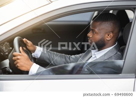 Side view of african american man in suit driving car Side view of african american man in suit driving car 69498600