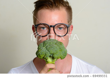 Portrait of young handsome man with eyeglasses holding broccoli 69499331