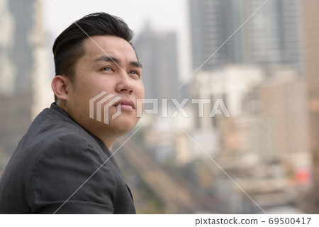 Closeup profile view of young overweight Asian businessman thinking in the city 69500417
