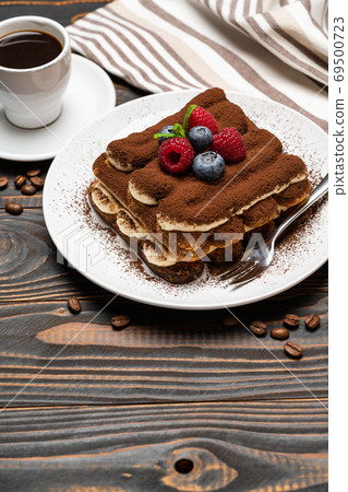 portion of Classic tiramisu dessert with raspberries, blueberries and cup of espresso coffee isolated on wooden background 69500723