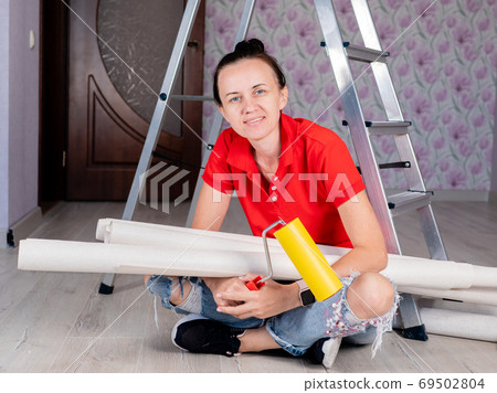 A woman in a room on the floor with rolls of Wallpaper in her hands. Concept renovation in the apartment, wallpapering in the room. A woman in a room on the floor with rolls of Wallpaper in her hands. Concept renovation in the apartment, wallpapering in the room. 69502804