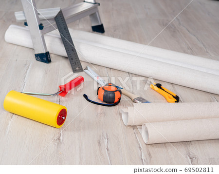 Close-up the measuring tape and the Wallpaper smoothing roller are lying on the floor next to the Wallpaper roll. Close-up the measuring tape and the Wallpaper smoothing roller are lying on the floor next to the Wallpaper roll. 69502811