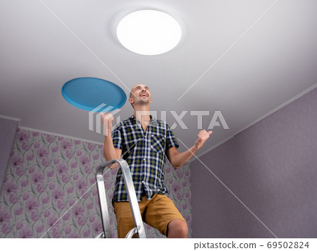 A happy man on a stepladder is happy that he has installed an led light on the ceiling. A happy man on a stepladder is happy that he has installed an led light on the ceiling. 69502824