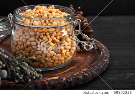 Pine nuts in a glass dish on a dark background with nuts scattered around Pine nuts in a glass dish on a dark background with nuts scattered around 69502828