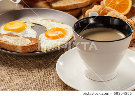Cup of black coffee, plate with fried eggs and toast with butter 69504896