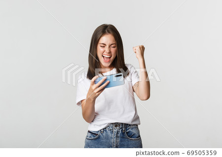 Rejoicing pretty girl playing mobile phone game and fist pump, satisfied with win Rejoicing pretty girl playing mobile phone game and fist pump, satisfied with win 69505359