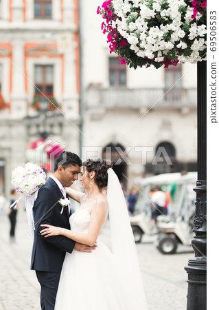Gorgeous happy couple standing close to each other and looking in eyes at old city background, wedding photo, European city, wedding day in Lviv 69506583