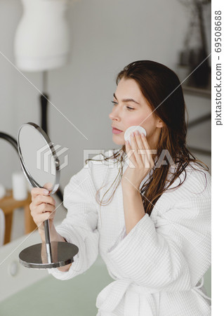 Beautiful young woman using cosmetic sponge and looking at mirror. 69508688