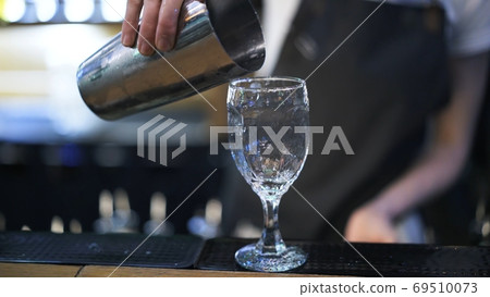 Bartender holding metal cup to pour cocktail into a glass 69510073