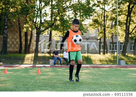 Concentrated skillful teen football player stuffs soccer ball on leg. Practicing sport exercises at artificial stadium. Concentrated skillful teen football player stuffs soccer ball on leg. Practicing sport exercises at artificial stadium. 69511556
