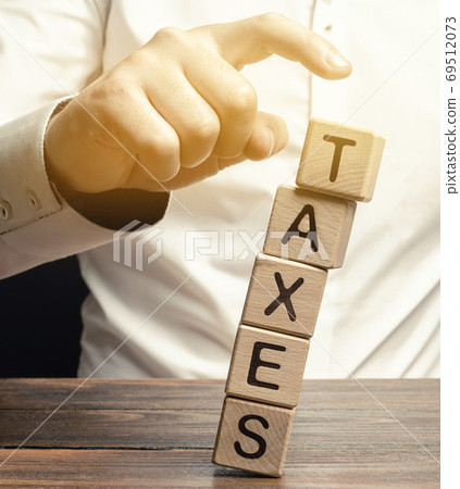 Businessman removes wooden blocks with the word Taxes. The concept of tax payment for housing and property. Income / goods tax. Avoidance. Burden Taxation. GST. Business and Finance. Selective focus Businessman removes wooden blocks with the word Taxes. The concept of tax payment for housing and property. Income / goods tax. Avoidance. Burden Taxation. GST. Business and Finance. Selective focus 69512073
