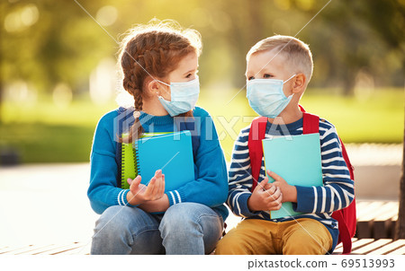 Little schoolkids in protective masks sitting on street Little schoolkids in protective masks sitting on street 69513993
