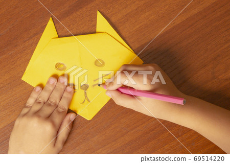The boy makes an origami cat from a yellow sheet of paper The boy makes an origami cat from a yellow sheet of paper 69514220