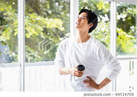 Young man standing by the window with a takeaway cup 69514709