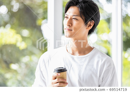 Young man standing by the window with a takeaway cup 69514719