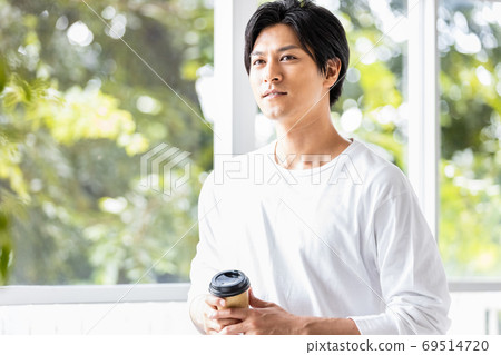 Young man standing by the window with a takeaway cup Young man standing by the window with a takeaway cup 69514720