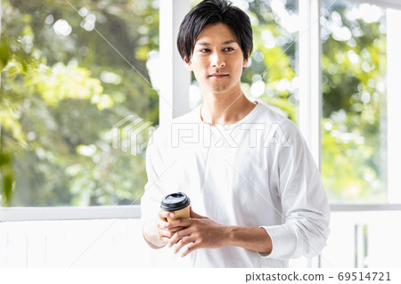 Young man standing by the window with a takeaway cup Young man standing by the window with a takeaway cup 69514721