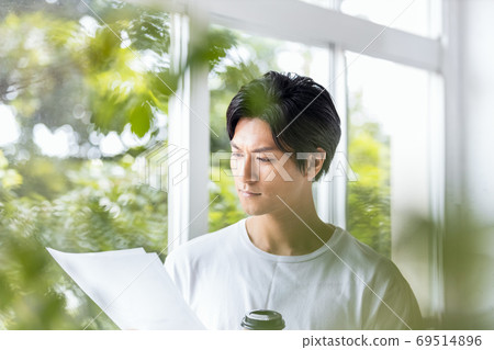 A man holding a takeaway cup and looking down at a paper document A man holding a takeaway cup and looking down at a paper document 69514896