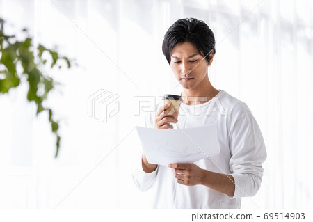 A man holding a takeaway cup and looking down at a paper document 69514903