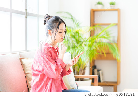 A woman who operates a smartphone while relaxing on the sofa. 69518181