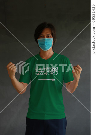 Masked man wearing Saudi Arabia flag color of shirt and standing 69521439
