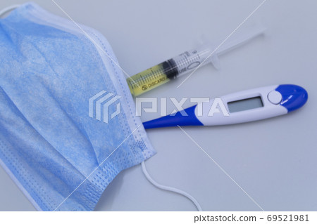 Focus on medical mask.Syringe, protective mask and electronic thermometer on a grey background.Vaccination against the virus. Focus on medical mask.Syringe, protective mask and electronic thermometer on a grey background.Vaccination against the virus. 69521981