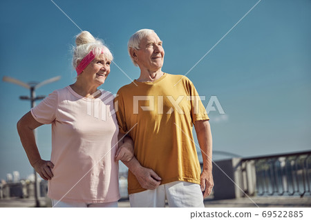 Two smiling pleased aged people standing outside Two smiling pleased aged people standing outside 69522885